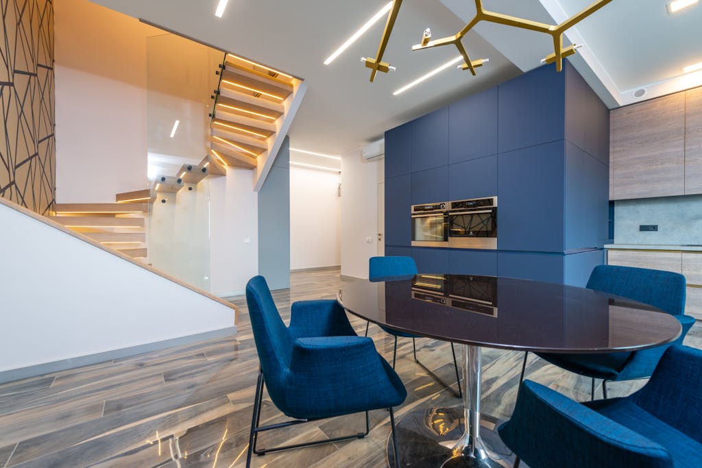 A spacious, modern kitchen with blue accents and a stylish staircase creating a sleek interior design.