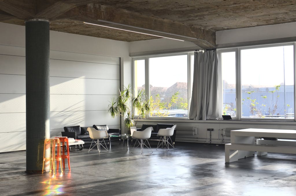 Interior of modern spacious room with column and couches placed near big window with curtains near table in light studio